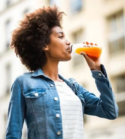 Close up of someone laughing post workout, holding a green smoothie or fresh water, with clear skin and bright eyes.